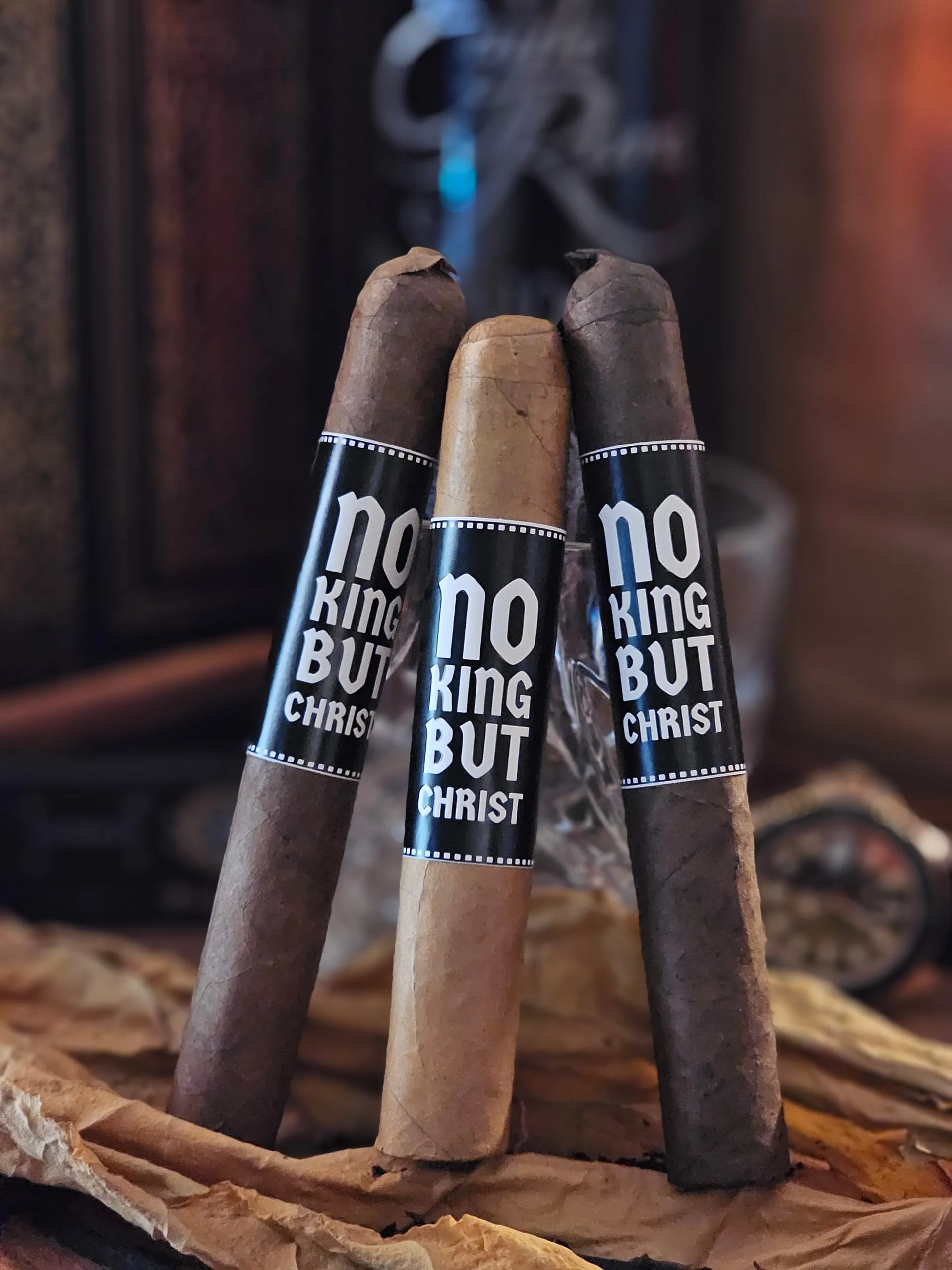 Three cigars standing on brown paper with no king but Christ bands